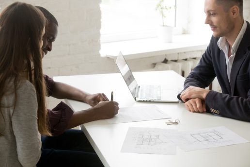 Interracial couple signing mortgage investment contract making real estate deal at meeting with broker realtor or financial advisor, happy family clients customers taking bank loan buying new house